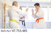 Determined motivated senior man wearing kimono working on hand strikes and martial arts skills in sparring with young opponent during group training. Стоковое видео, видеограф Яков Филимонов / Фотобанк Лори