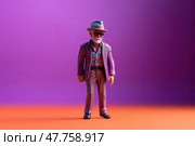 Miniature figure model toy of carefree extravagant elderly man in sunglasses, fedora and blue suit on purple background. Стоковое AI-изображение, AI-художник Данила Большаков / Фотобанк Лори