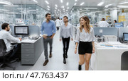 Young woman in white shirt and black shorts walks across office open space. Two men behind are out of focus. Intentional motion blur. Scientific workplace. AI-generated item. Стоковое AI-изображение, AI-художник Катерина Ковалева / Фотобанк Лори