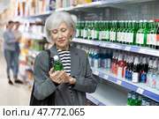 Senior lady choosing bottle of Korean soju at local liquor store. Стоковое фото, фотограф Яков Филимонов / Фотобанк Лори