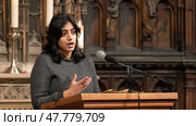 A woman stands confidently at a podium, engaging with the audience as she speaks into a microphone. Стоковое AI-изображение, AI-художник Данила Большаков / Фотобанк Лори