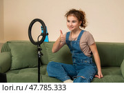 Young female blogger sits on a sofa looking at a phone attached to a ring light. Стоковое фото, фотограф Мария Мороз / Фотобанк Лори