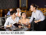 Waitress helps to sort out menu, choose original dish to young married couple. Стоковое фото, фотограф Яков Филимонов / Фотобанк Лори
