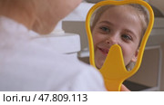 Lovely little girl looking in the mirror at her teeth after teeth surgery in a pediatric stomatology. A little girl sits in a dental chair and examines her cured teeth while looking in the mirror. Стоковое видео, видеограф Ирина Михайличенко / Фотобанк Лори