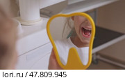 Lovely little girl looking in the mirror at her teeth after teeth surgery in a pediatric stomatology. A little girl sits in a dental chair and examines her cured teeth while looking in the mirror. Стоковое видео, видеограф Ирина Михайличенко / Фотобанк Лори