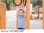 Lifestyle. A cute little boy is hanging on rings on a sports field in the fresh air. The concept of children's sports and physical development. Стоковое фото, фотограф Photojuli / Фотобанк Лори