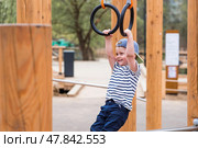 Lifestyle. A cute little boy is hanging on rings on a sports field in the fresh air. The concept of children's sports and physical development. Стоковое фото, фотограф Photojuli / Фотобанк Лори