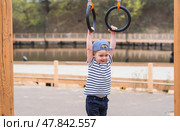 Lifestyle. A cute little boy is hanging on rings on a sports field in the fresh air. The concept of children's sports and physical development. Стоковое фото, фотограф Photojuli / Фотобанк Лори