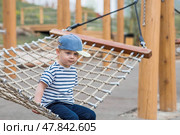 Lifestyle. A cute little boy is sitting in a hammock on a modern outdoor playground. The concept of family entertainment and leisure. Стоковое фото, фотограф Photojuli / Фотобанк Лори