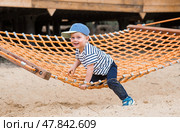 Lifestyle. A cute little boy is sitting in a hammock on a modern outdoor playground. The concept of family entertainment and leisure. Стоковое фото, фотограф Photojuli / Фотобанк Лори