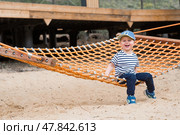 Lifestyle. A cute little boy is sitting in a hammock on a modern outdoor playground. The concept of family entertainment and leisure. Стоковое фото, фотограф Photojuli / Фотобанк Лори