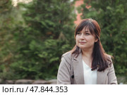 With a calm expression, a woman enjoys a peaceful moment outdoors in a verdant park. The surrounding nature creates a serene backdrop, enhancing her thoughtful demeanor and stylish attire. Стоковое фото, фотограф Aleksandr Golubev / Фотобанк Лори