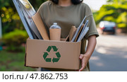 A Girl in plain colors T-shirt carries a box of recyclables. Стоковое AI-изображение, AI-художник Ирина Ручушкина / Фотобанк Лори