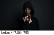 Intense lowkey portrait of a mysterious figure in a hooded sweatshirt with light skin tone pointing towards the camera. Стоковое AI-изображение, AI-художник Андрей Бакусов / Фотобанк Лори