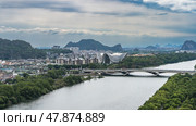 Panorama of a modern city. View from the height. Automobile bridge over the river. Green vegetation on the shores. Lots of multi-storey buildings. A theater with a curved roof. Mountains. Sky, clouds. Стоковое фото, фотограф Вера Ивановна Кубарева / Фотобанк Лори
