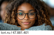 A girl with curly hair and glasses smiles endearingly while sitting indoors, promoting a sense of warmth and openness in a friendly environment. Стоковое AI-изображение, AI-художник Данила Большаков / Фотобанк Лори