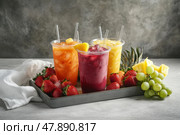 Assortment of cold-pressed juices in a tray among gray wall. glasses of juices. Ripe fresh fruit ingredients on table. Fresh various smoothie vegetable and fruit juices drinking glass. Стоковое AI-изображение, AI-художник Марина Демидюк / Фотобанк Лори
