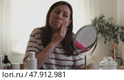 Attractive brunette mid adult woman putting on makeup looking in the mirror. Beautiful lady caring her face. 40 years old female applied cosmetics. Natural beauty and aging concept. Skin care, make-up. Стоковое видео, видеограф Марина Демидюк / Фотобанк Лори