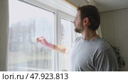 Man is cleaning window in apartment. Adult Male cleaner using a squeegee to wash a window. Bearded guy wiping and washing glasses with with spray bottle, rag and vacoom. Everyday chores. Purification. Стоковое видео, видеограф Марина Демидюк / Фотобанк Лори