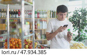 Young guy using smartphone to scan and and compare two grounded herbal spices in supermarket aisle, comparing prices, ingredients, and online reviews to choose best option for gastronomic treat. Стоковое видео, видеограф Яков Филимонов / Фотобанк Лори
