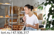 Pleased middle-aged Asian woman chooses some pastry from rack in bakery shop. Стоковое видео, видеограф Яков Филимонов / Фотобанк Лори