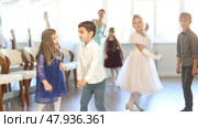 Group of cheerful expressive tweens, girls ad boys in formal wear dancing energetic twist dance in sunlit classroom during children festive event. Стоковое видео, видеограф Яков Филимонов / Фотобанк Лори