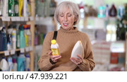 Elderly woman chooses products to care for gray hair. European woman chooses shampoo and mask to nourish aging hair. Стоковое видео, видеограф Яков Филимонов / Фотобанк Лори