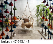 Cozy indoor seating area featuring a macrame hanging chair surrounded by colorful decorative elements and greenery. Стоковое фото, фотограф Кривошеина Елена Леонидовна / Фотобанк Лори