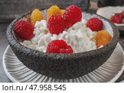 Creamed cottage cheese with raspberries. An easy healthy breakfast. A bowl filled with grainy, creamy cottage cheese is garnished with bright yellow and red raspberries. Close-up. Стоковое фото, фотограф Оксана Медведева / Фотобанк Лори