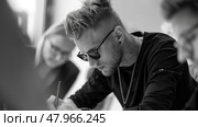 A tattooed man wearing sunglasses focuses intently on signing documents amidst a group discussion at a table. Стоковое AI-изображение, AI-художник Данила Большаков / Фотобанк Лори