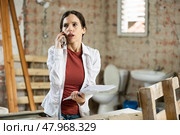 Confused woman with papers talking on phone in apartment during renovations. Стоковое фото, фотограф Яков Филимонов / Фотобанк Лори