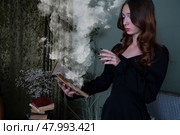 An Enchanting Sorceress is deeply engrossed in reading a Spellbook surrounded by swirling, Mystical Smoke. Стоковое фото, фотограф Anastasy Yarmolovich / Фотобанк Лори