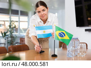 Positive young woman putting flag of Argentina on the table with flag of Brazil in conference room. Стоковое фото, фотограф Яков Филимонов / Фотобанк Лори