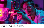 A scientist carefully adjusts equipment amidst vibrant lab lighting during an evening research session. Стоковое AI-изображение, AI-художник Данила Большаков / Фотобанк Лори