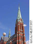 Stockholm. Sweden. Церковь Святого Иоанна в солнечный день. Готическая церковь Святого Иоанна ( Санкт Йоханнес Кирка) в Стокгольме с краснокирпичным фасадом и зелёным медным шпилем возвышается на фоне Готическая церковь Святого Иоанна (Санкт Йоханнес Кирка) в Стокгольме с краснокирпичным фасадом и зелёным медным шпилем возвышается на фоне ярко-синего неба. Архитектурные детали подчёркнуты контрастным освещением — классический пример неоготики в Швеции. Стоковое фото, фотограф Анна Чижова / Фотобанк Лори