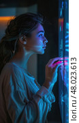 A woman touches a glowing touchscreen, captivated by the vibrant colors in a darkened space. Стоковое AI-изображение, AI-художник Данила Большаков / Фотобанк Лори