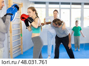 Teen girl in boxing gloves practices punches with trainer in mitts in sport club during family training. Стоковое фото, фотограф Яков Филимонов / Фотобанк Лори