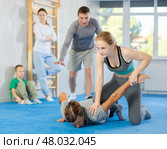 At self-defense training, trainer teaches teenage girl technique of grabbing arm and lowering opponent to floor. Стоковое фото, фотограф Яков Филимонов / Фотобанк Лори
