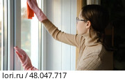 Teen girl is cleaning window in apartment. Teenager female cleaner using a squeegee to wash a window. Girl wiping, washing glasses with with spray bottle, rag and vacoom. Everyday chores. Purification. Стоковое видео, видеограф Марина Демидюк / Фотобанк Лори