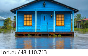 A bright blue house stands partially submerged in floodwaters, with yellow-lit windows reflecting on the water's surface in a cloudy atmosphere. Стоковое AI-изображение, AI-художник Данила Большаков / Фотобанк Лори
