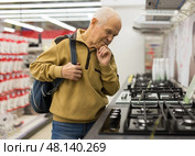 Senor man pensioner buying kitchen stove in showroom of electrical appliance store. Стоковое фото, фотограф Татьяна Яцевич / Фотобанк Лори