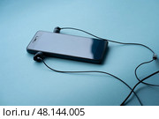 Черный мобильный телефон и черные проводные наушники на голубом фоне. Стоковое фото, фотограф Татьяна Шестернева / Фотобанк Лори