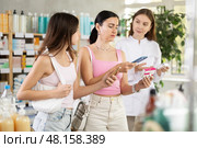 Family of mother and daughter clients choosing box of paracetamol antipyretic pills, scan QR code on label, looking at composition of medicine in drug store, young professional woman pharmacist offering goods and helping with selection. Стоковое фото, фотограф Яков Филимонов / Фотобанк Лори
