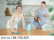 Adult daughter and mum veste tidy up the room - daughter dusts the table, mum vacuums room. Стоковое фото, фотограф Яков Филимонов / Фотобанк Лори
