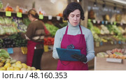 Woman seller take inventory with list in vegetable shop. Стоковое видео, видеограф Яков Филимонов / Фотобанк Лори