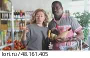 African man with European wife hold bottle and choose alcohol wine bottle in storeEuropean woman with African husband took different varieties of alcohol from shelf, choose wine light alcohol beverage. Client hesitates before buying, chooses alcohol, reads labels on bottles. Стоковое видео, видеограф Яков Филимонов / Фотобанк Лори