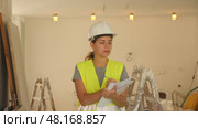 Woman foreman in a protective helmet and yellow vest checks the completed construction work on the drawing. Стоковое видео, видеограф Яков Филимонов / Фотобанк Лори