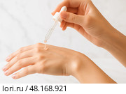 Woman applies hydrating facial serum drop onto back of hand with cosmetic pipette, demonstrating clean skincare routine for healthy radiant complexion. Стоковое AI-изображение, AI-художник Павел Муравьев / Фотобанк Лори