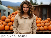 carefree young woman with curly hair шт beige long sleeve sweatshirt stands in front of a pile of pumpkins during harvest on a farm in autumn. Стоковое AI-изображение, AI-художник Данила Большаков / Фотобанк Лори