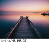 Morning breaks over the dock, painting the sky in vibrant colors as calm waters mirror the stunning display. The stillness invites reflection and peace at this picturesque location Generative AI. Стоковое AI-изображение, AI-художник Юлия Петровская / Фотобанк Лори